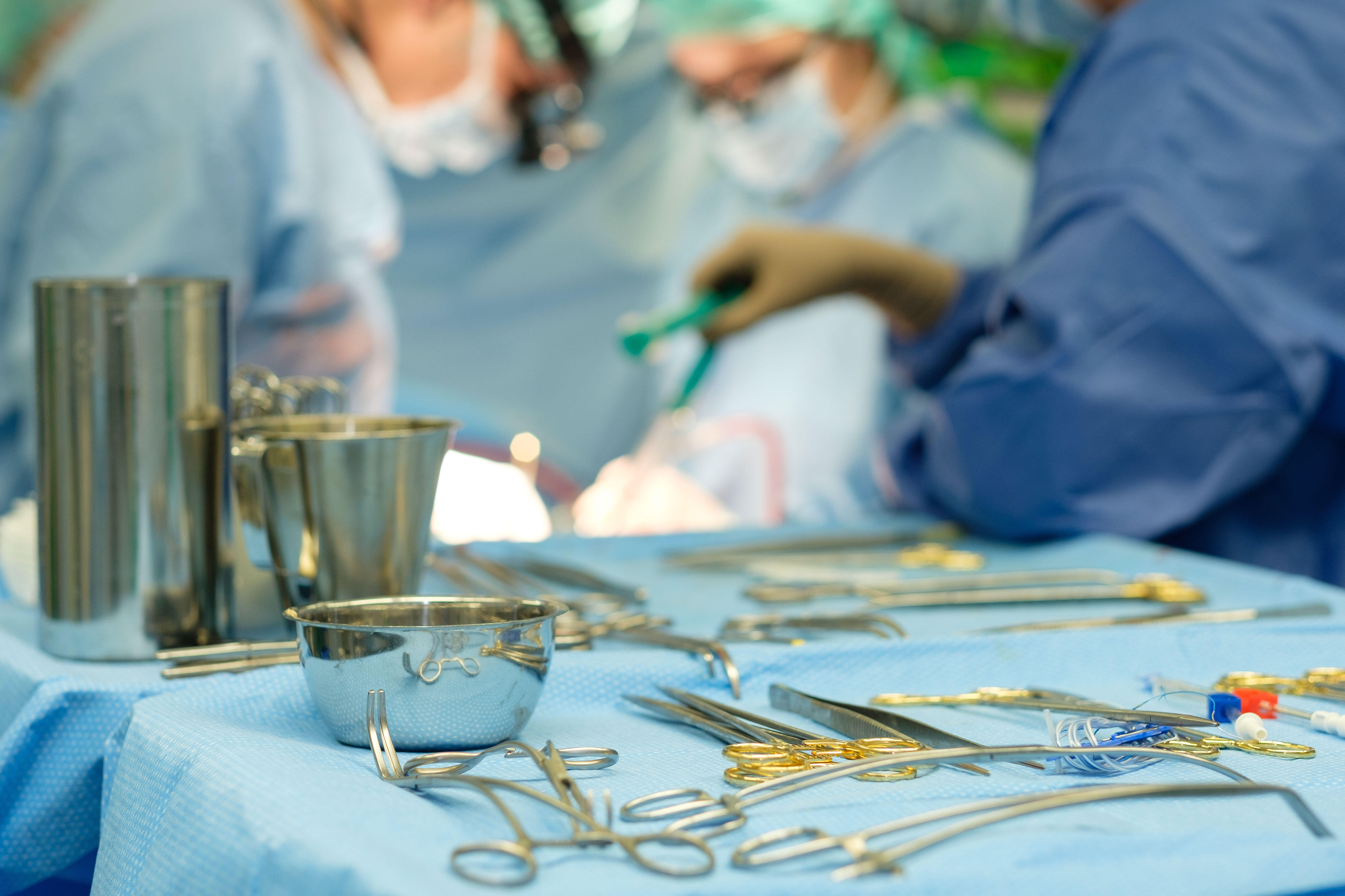 Instrumente für eine Herz-OP liegen auf einem Operationstisch, im Hintergrund sieht man operierende Ärzte