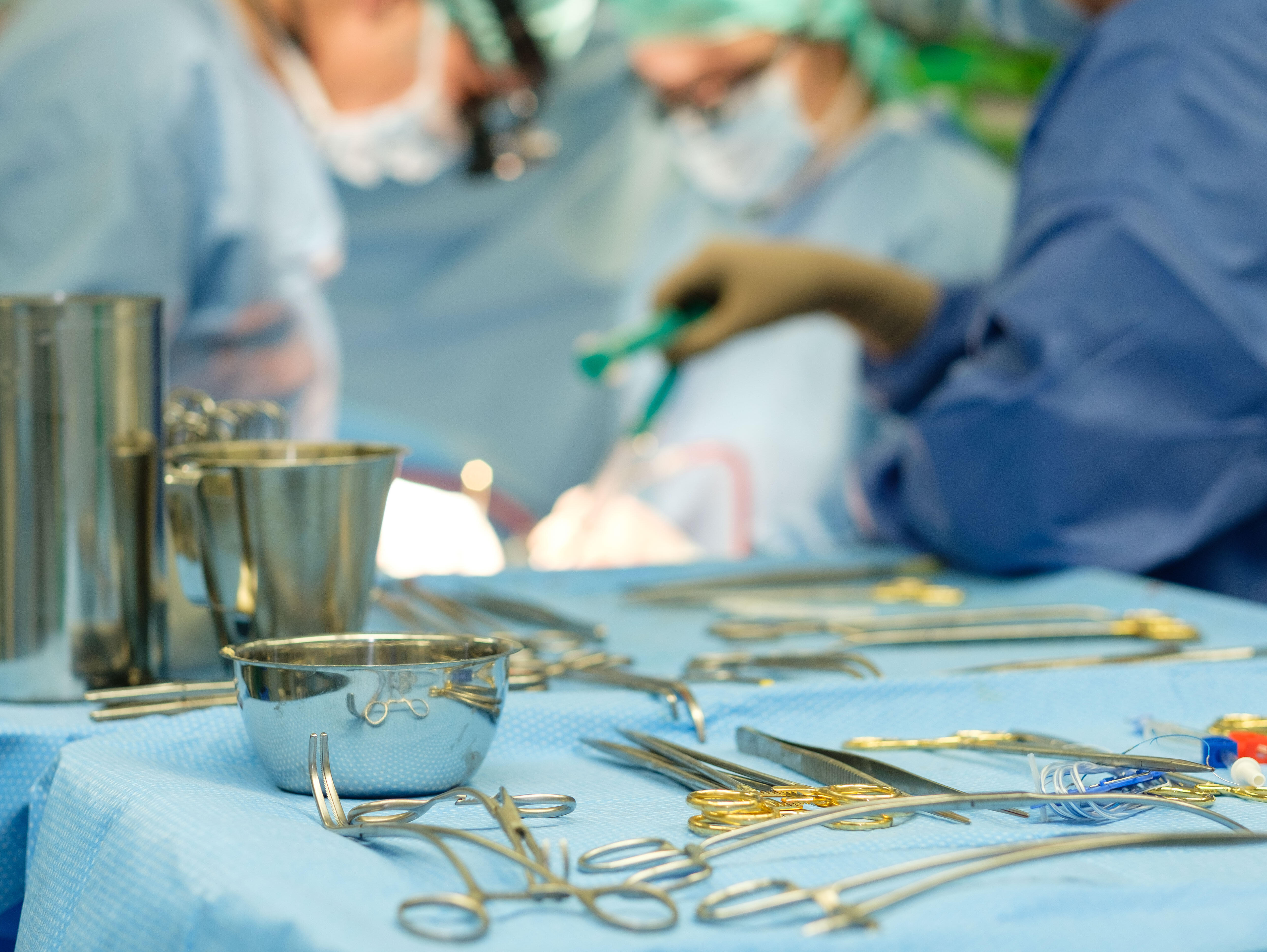 Instrumente für eine Herz-OP liegen auf einem Operationstisch, im Hintergrund sieht man operierende Ärzte